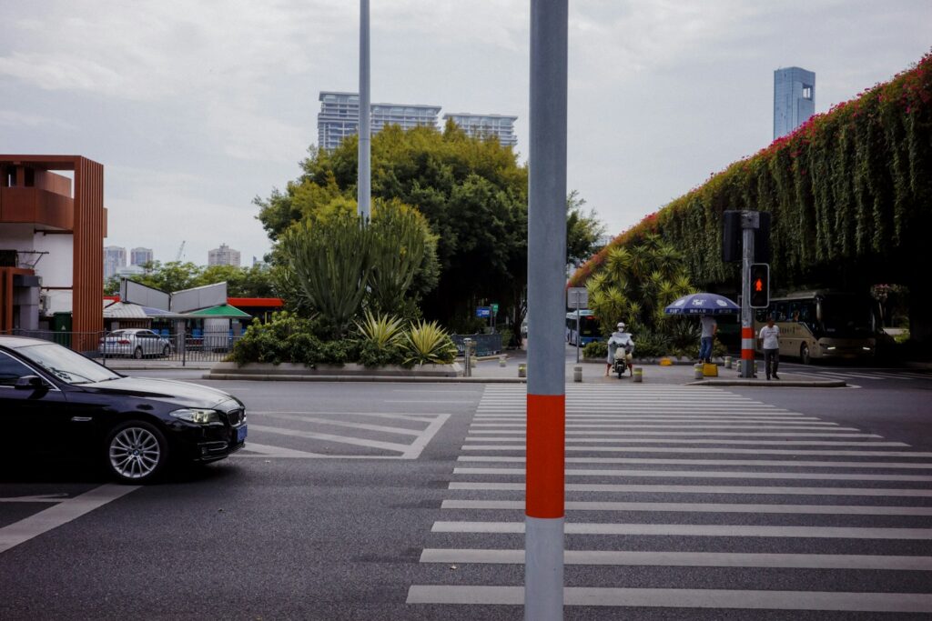 Urban street with a crosswalk, car, and green overpass.