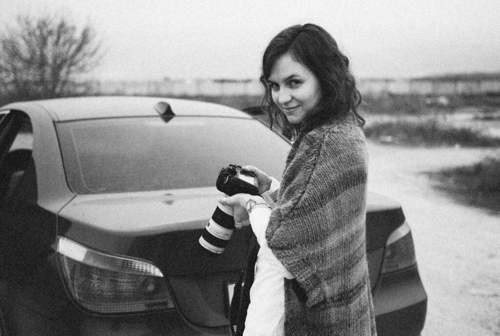 a woman standing next to a car holding a camera