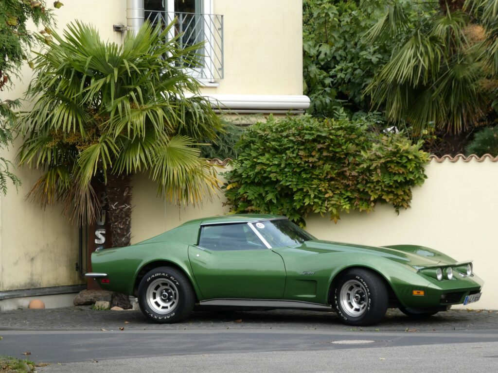 Green vintage car parked near palm trees and building