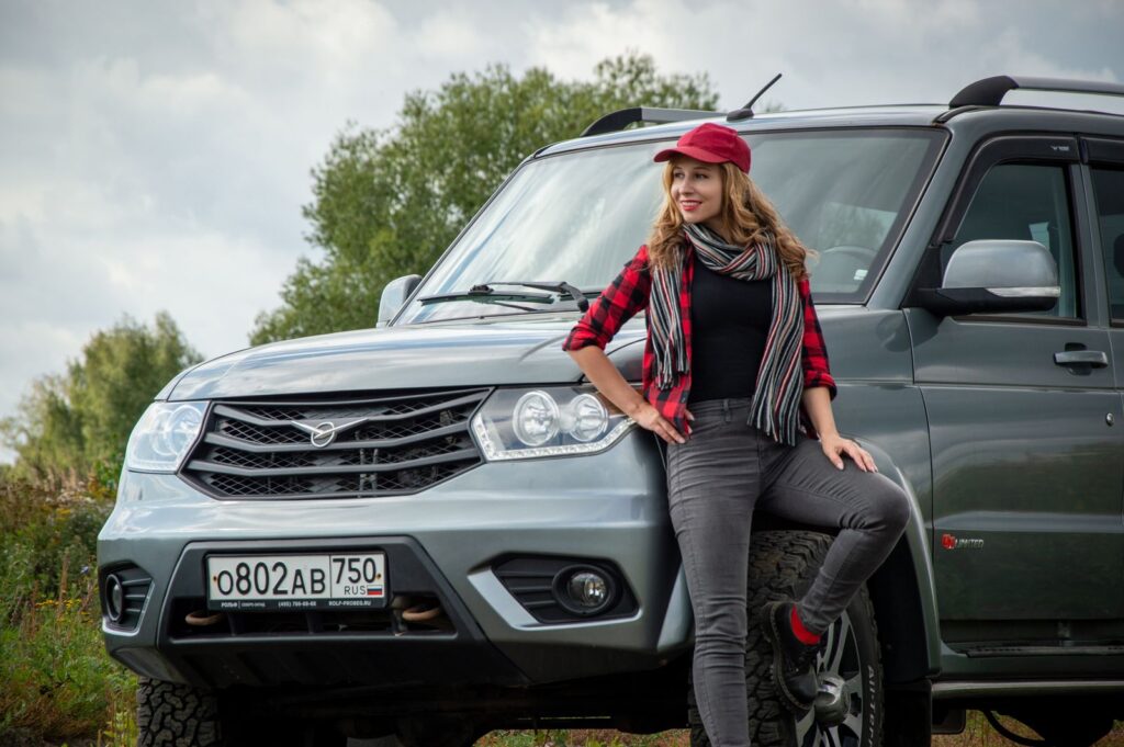 Smiling woman in red cap leaning on SUV with outdoor background.
