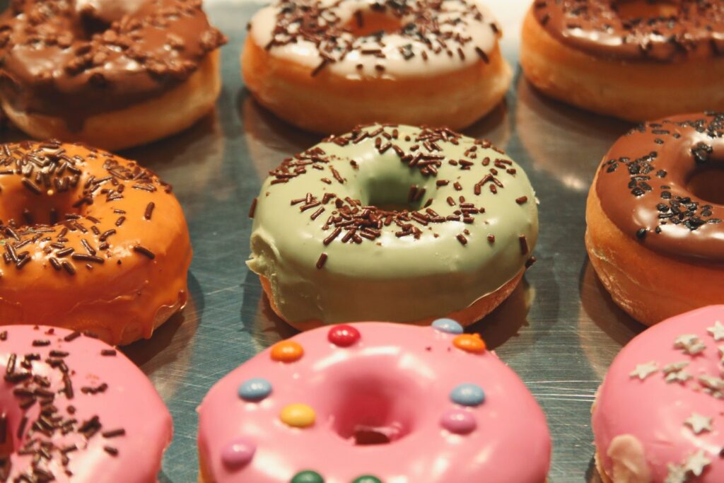 A close-up of various colorful iced donuts topped with chocolate sprinkles on a reflective surface.