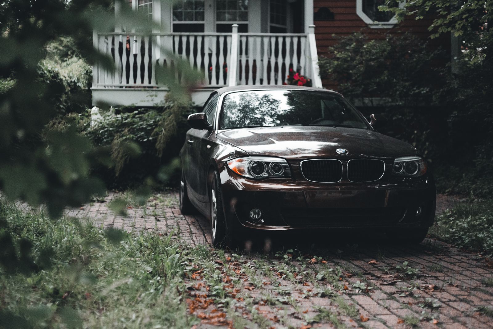 Black sedan parked on paved path amidst greenery and a wooden veranda.