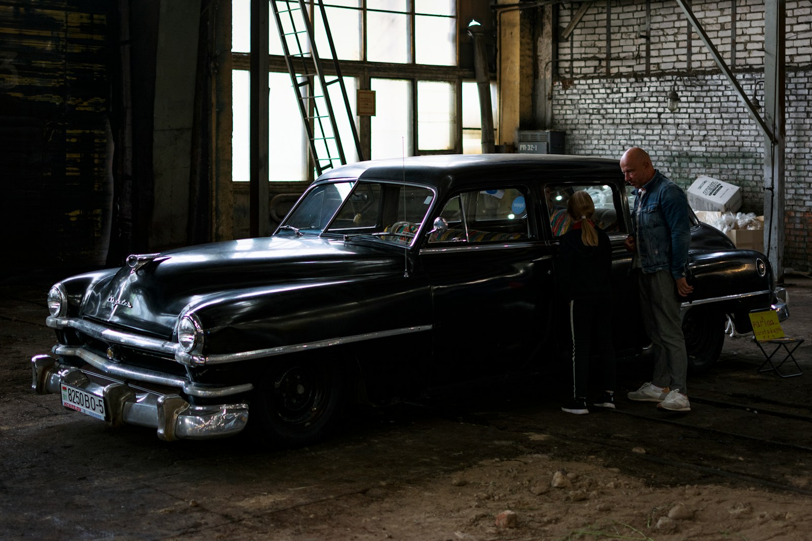 a man and a woman standing next to a car in a garage