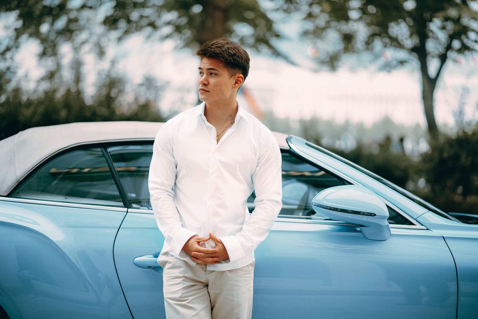 A man poses next to a light blue convertible.
