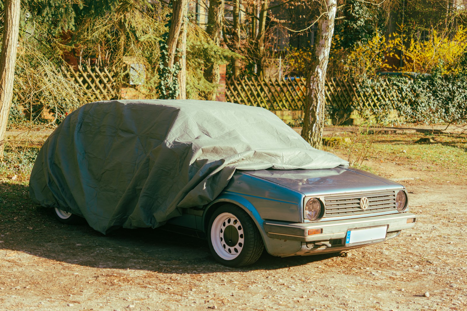 Car covered with a tarp in a wooded area.