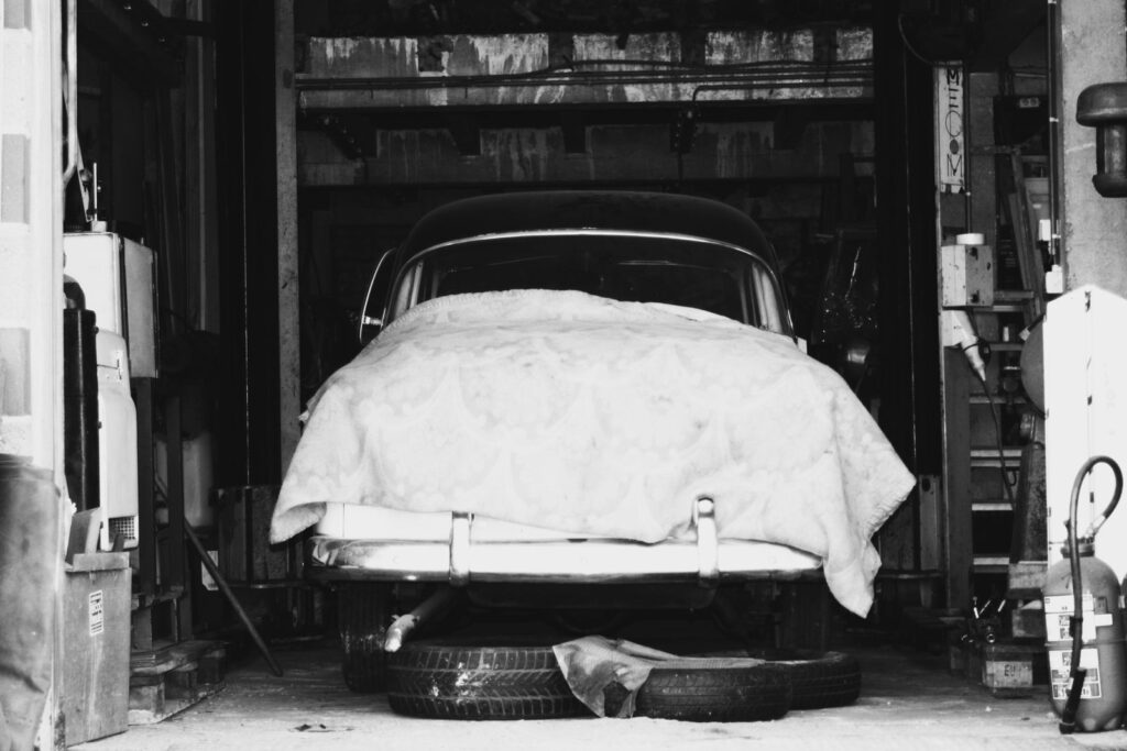 Black and white vintage car under a blanket in a garage workshop setting.