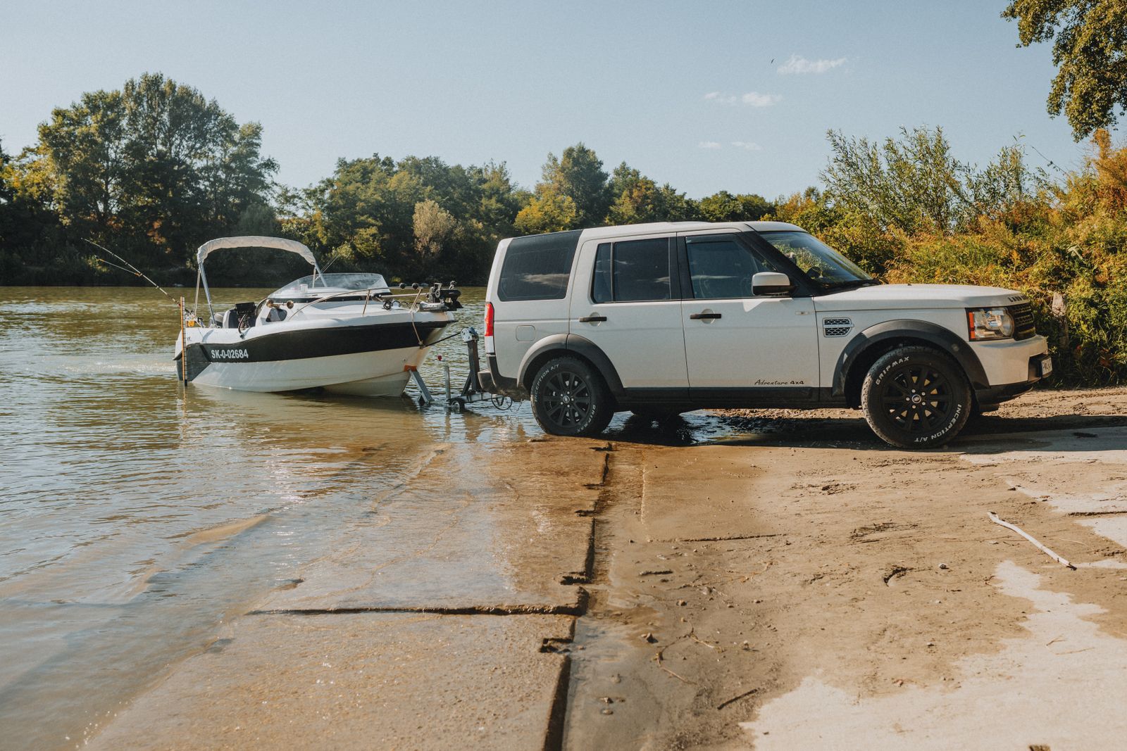 An SUV launching a speedboat into a river on a sunny day, showcasing outdoor adventure.