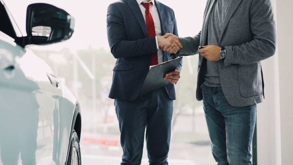Two men shaking hands in a car dealership, symbolizing a successful business deal.