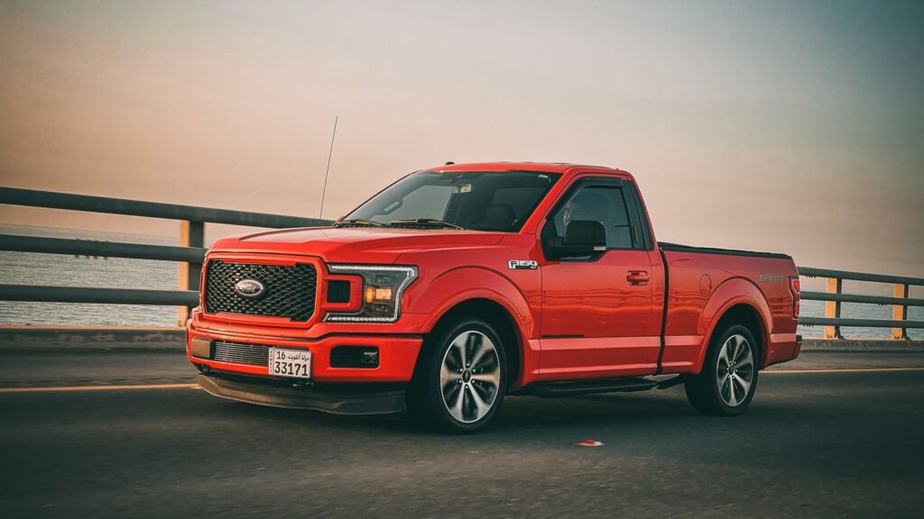 Red Ford F-150 truck driving on a bridge during sunset. Sleek and modern vehicle on the move.