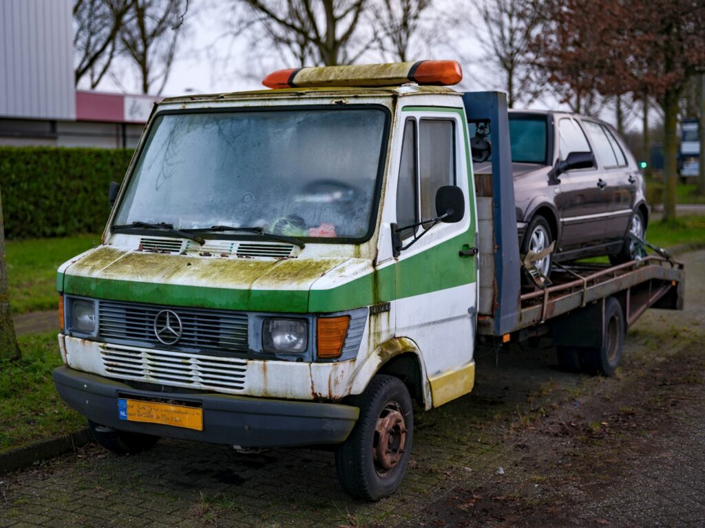 An old green and white van is being towed by a tow truck