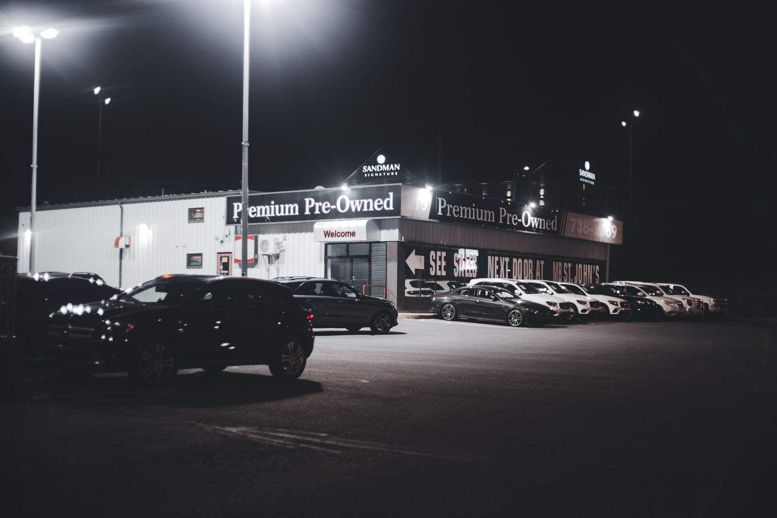 Illuminated car dealership lot showcasing premium pre-owned vehicles at night.