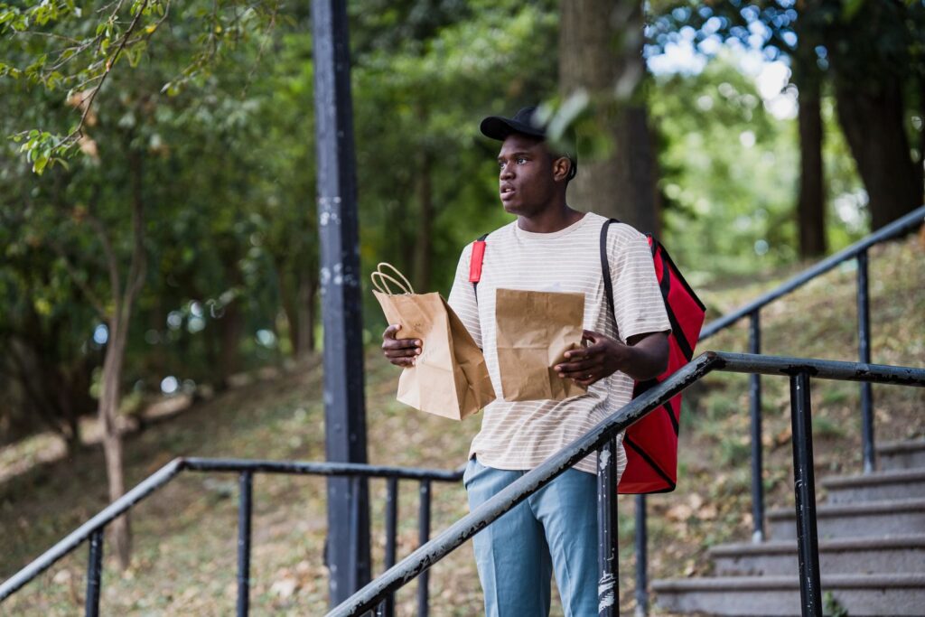 Young man delivering packages outdoors, standing on stairs with trees around.
