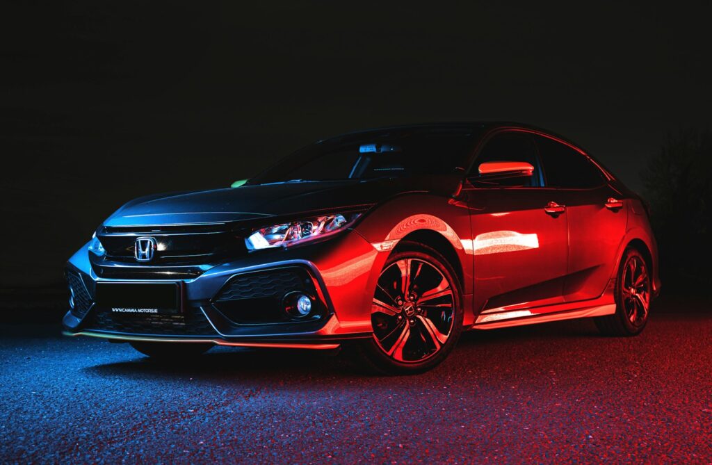 A Honda Civic sedan illuminated by blue and red light on asphalt at night