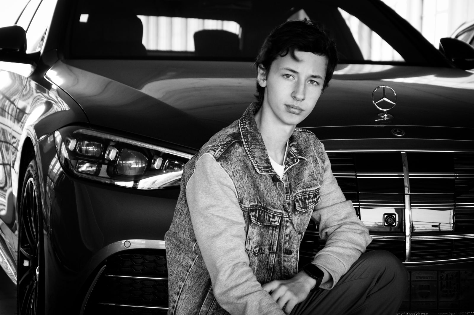 Teen crouching in front of a Mercedes-Benz, exuding luxury and style.