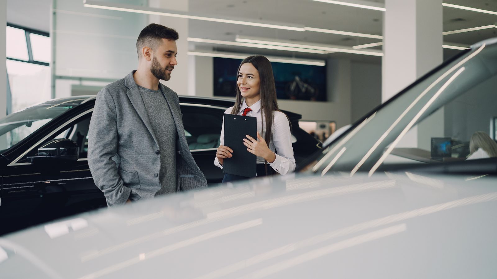 Man consults with salesperson in modern car dealership showroom.