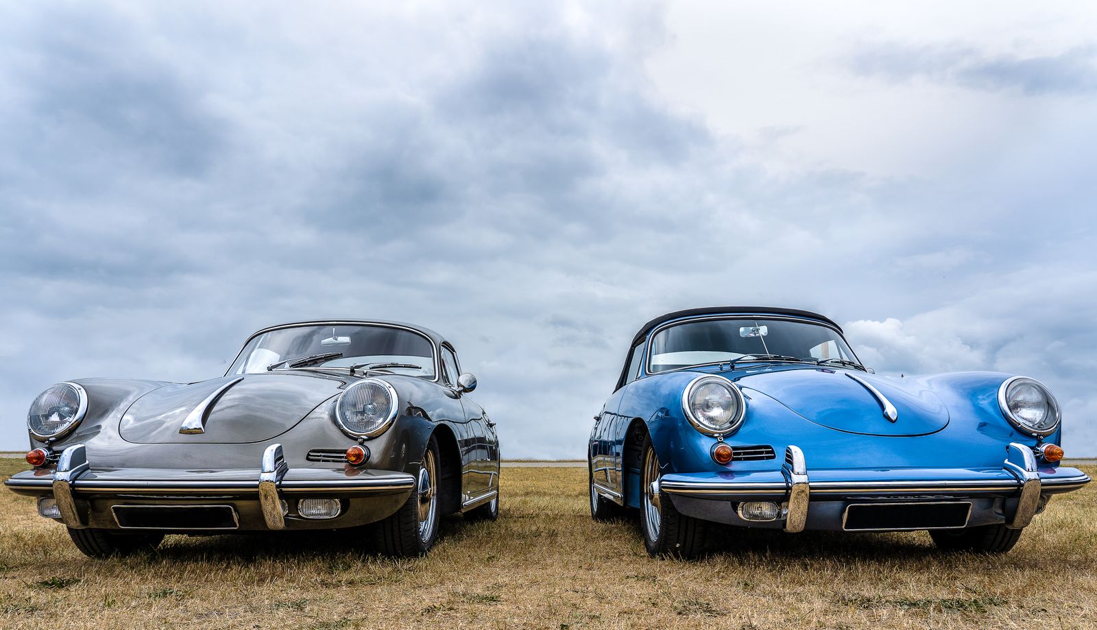 Two vintage classic cars showcased outdoors on a cloudy day, highlighting their timeless design.