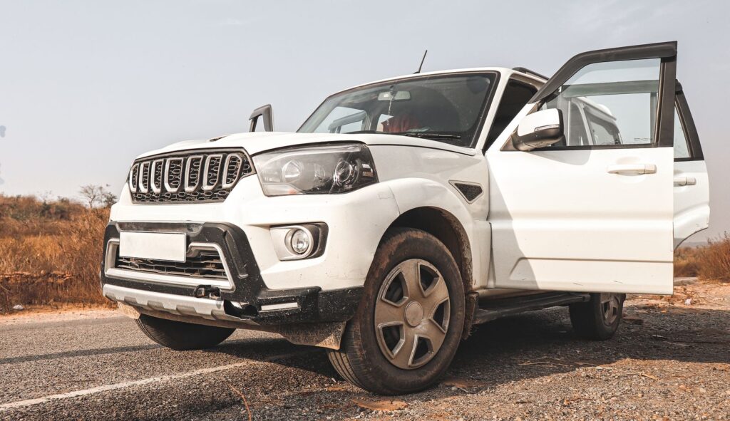 A white SUV parked on a rural road in India, showcasing its grille and open doors.