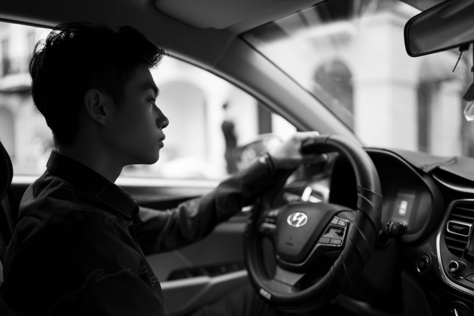 Black and white contemplative young ethnic male driving powerful contemporary car along city street