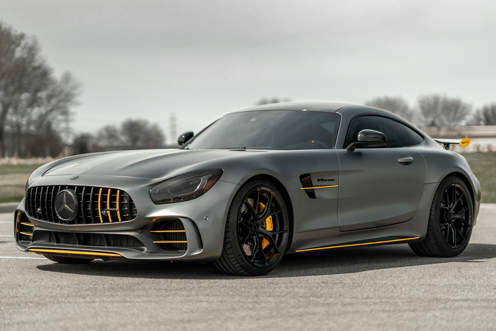 A matte grey sports car with yellow accents parked on an asphalt surface