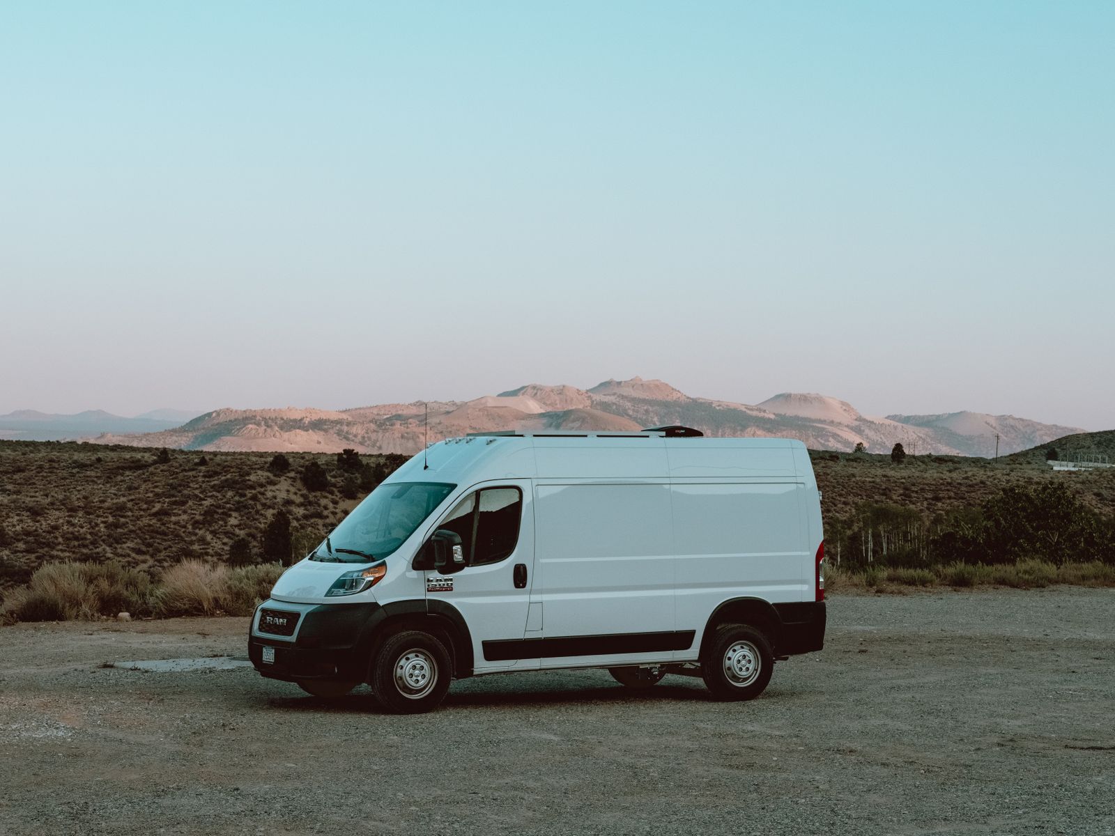 A white van parked outdoors against a backdrop of mountains and clear blue sky.