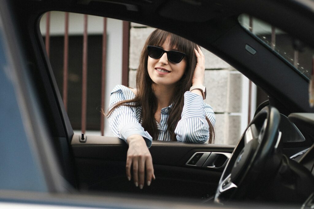 A stylish woman smiles while leaning out of car.