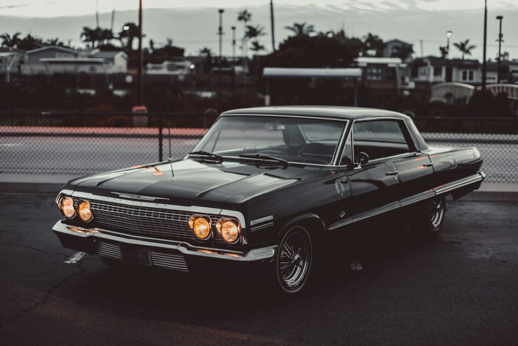 A black Chevrolet Impala with glowing headlights parked on an asphalt lot