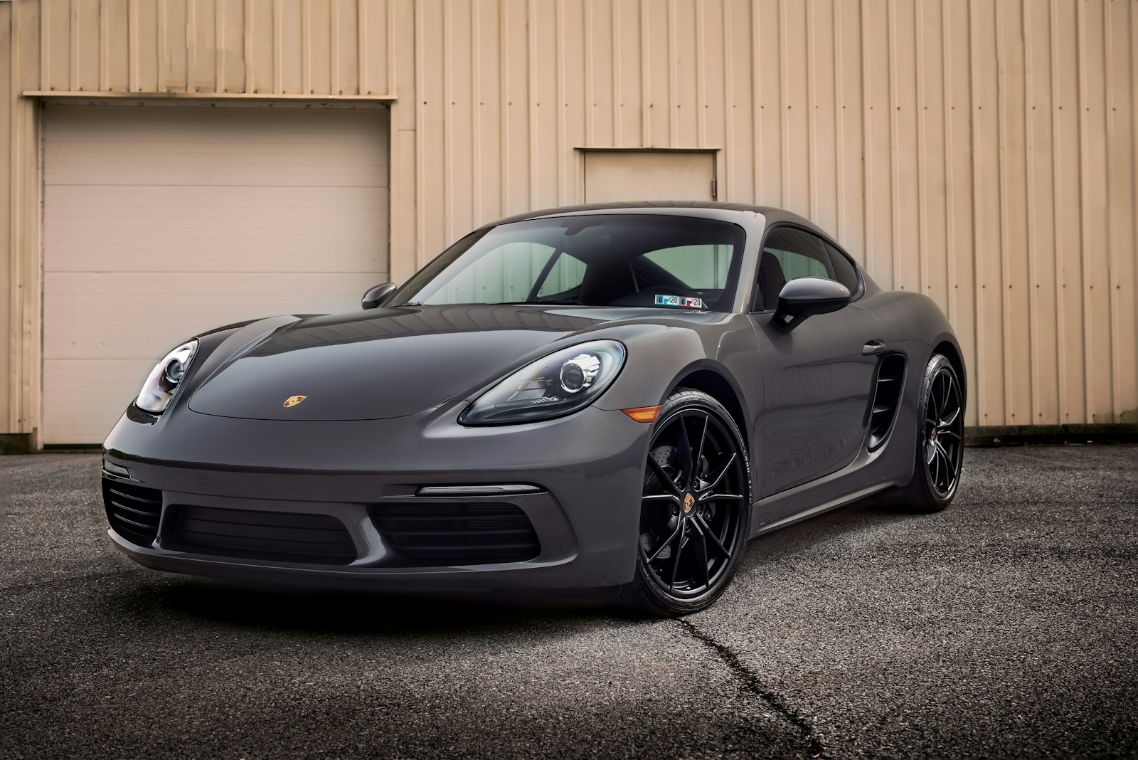 A grey Porsche sports car parked on asphalt in front of a metal building