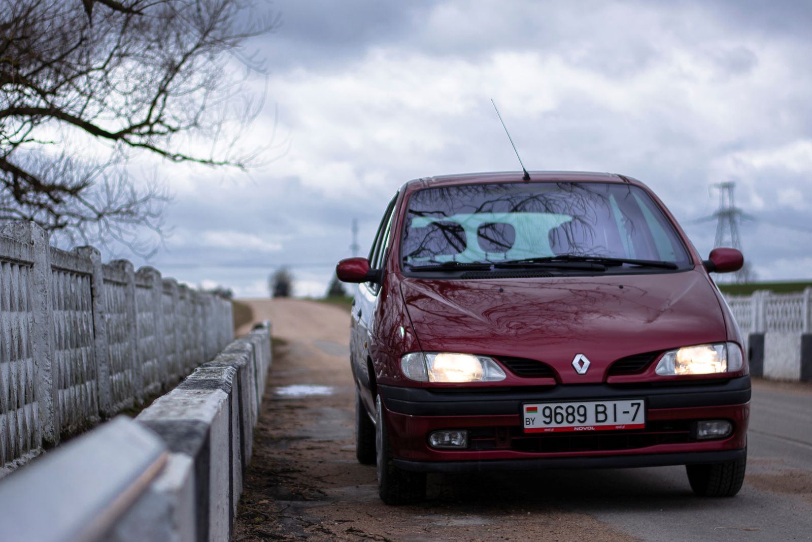 Red Renault parked on a quiet countryside road under a cloudy sky.