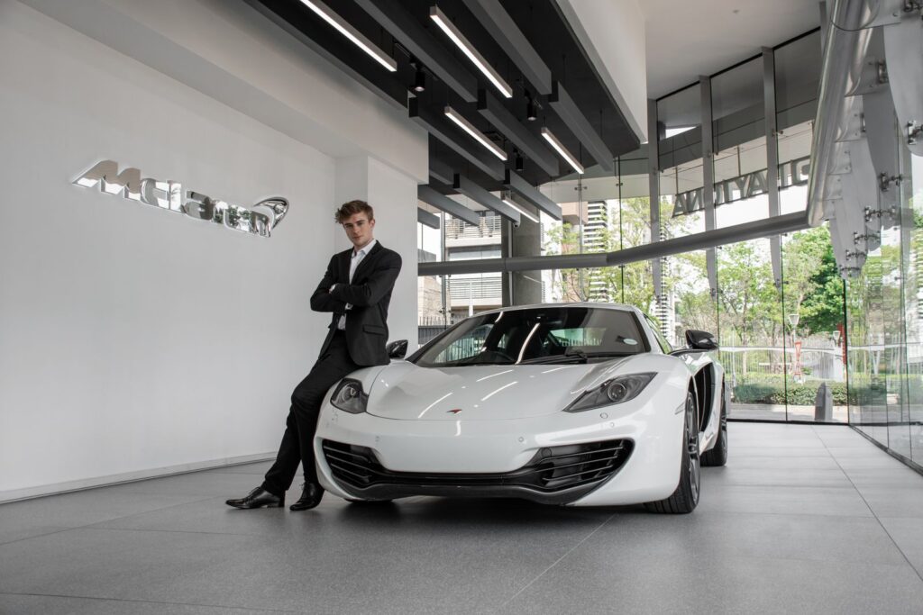 A stylish male model poses confidently with a sleek white sports car in an elegant car dealership showroom.