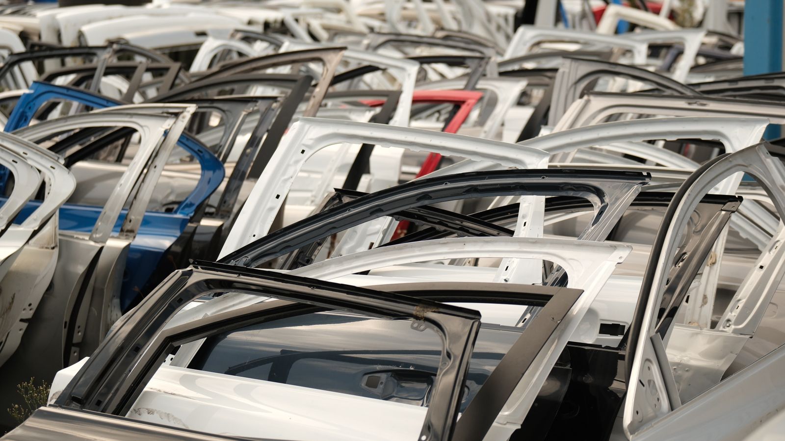 A variety of car doors in different colors arranged in a junkyard setting.