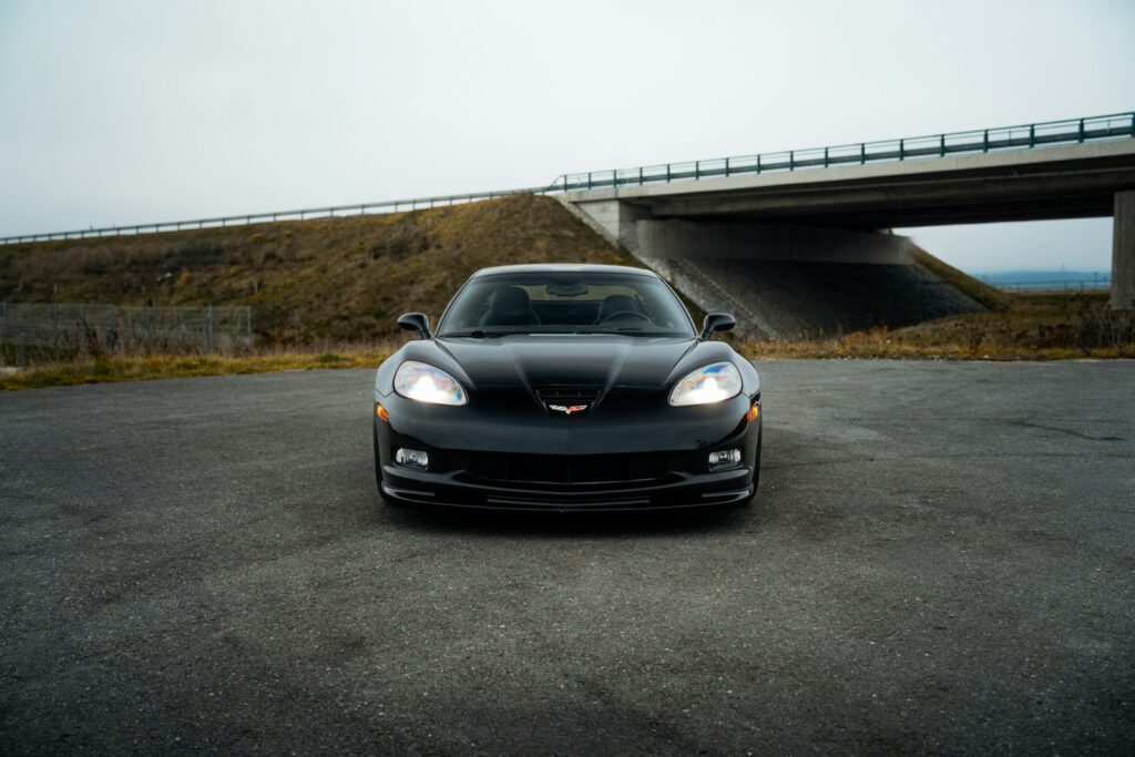 A black car parked in a parking lot next to a bridge