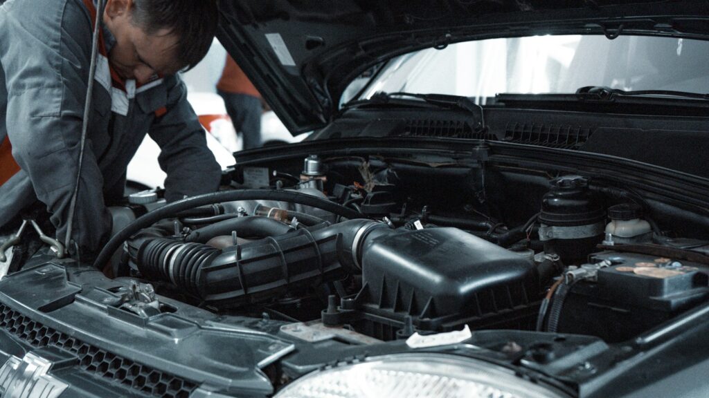 A mechanic in a grey uniform inspecting the engine of a car