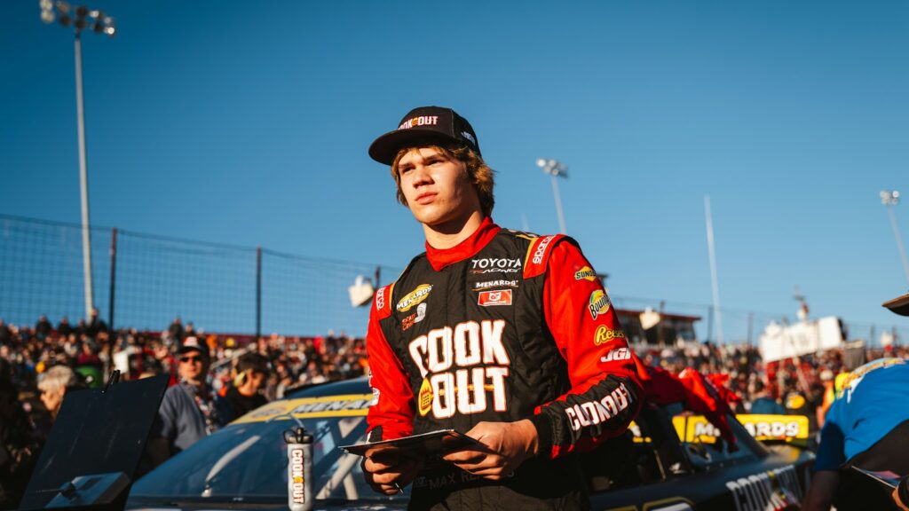 Young race car driver in uniform with crowd behind him