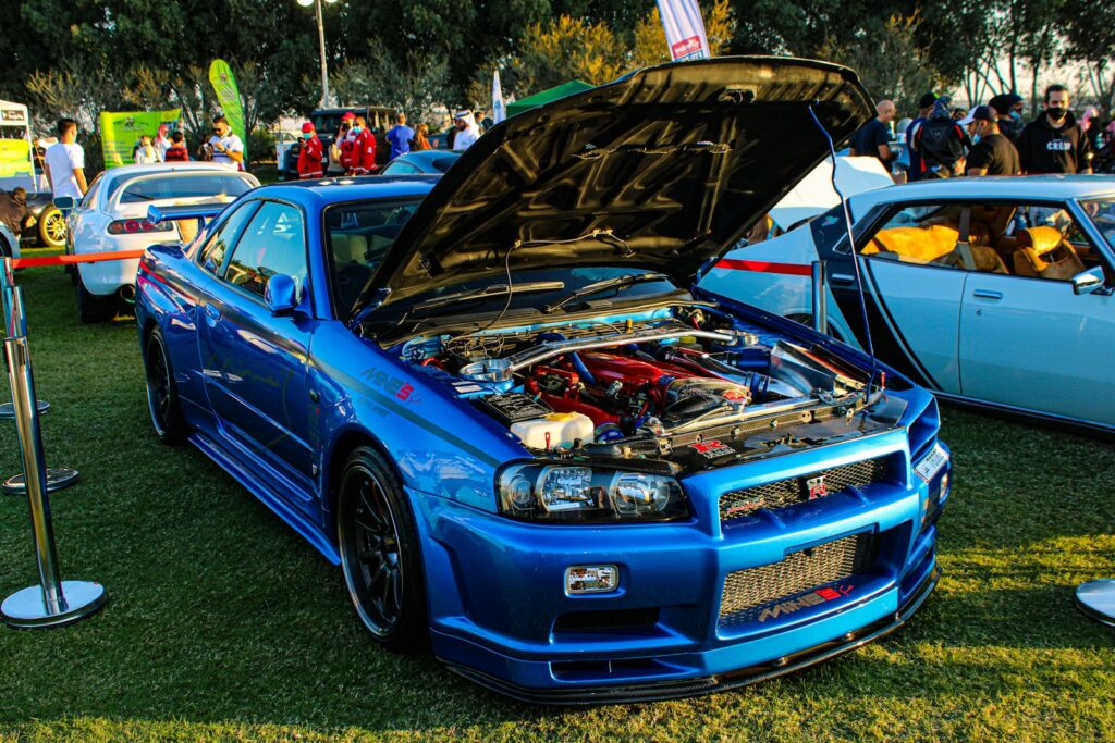 A blue Nissan Skyline GT-R with an open hood at an outdoor car show