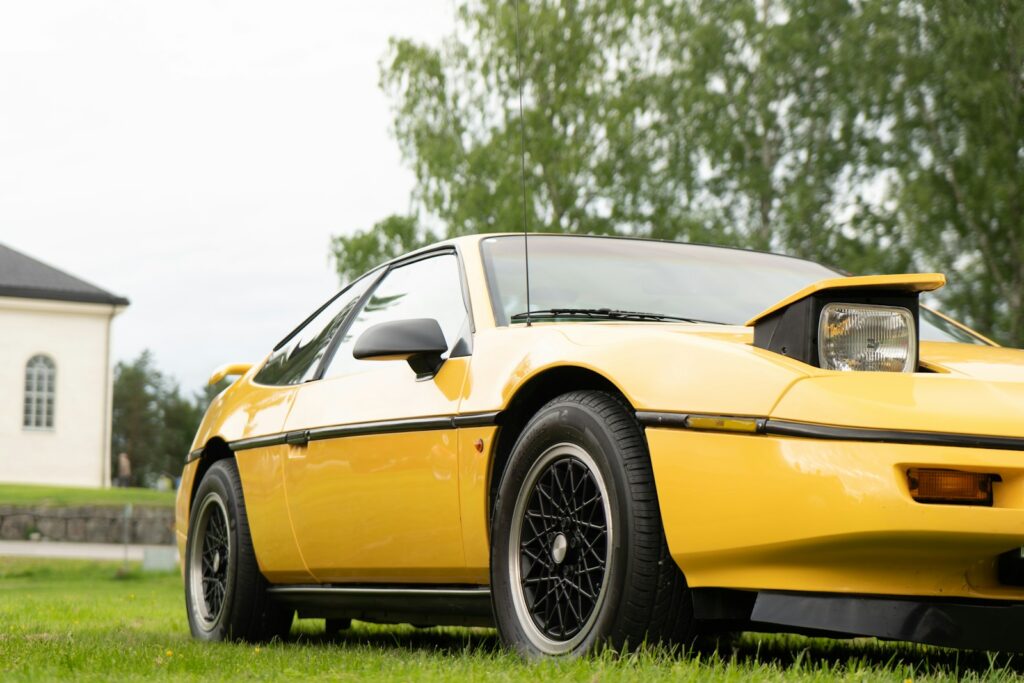 A yellow sports car with pop-up headlights parked on a grassy field