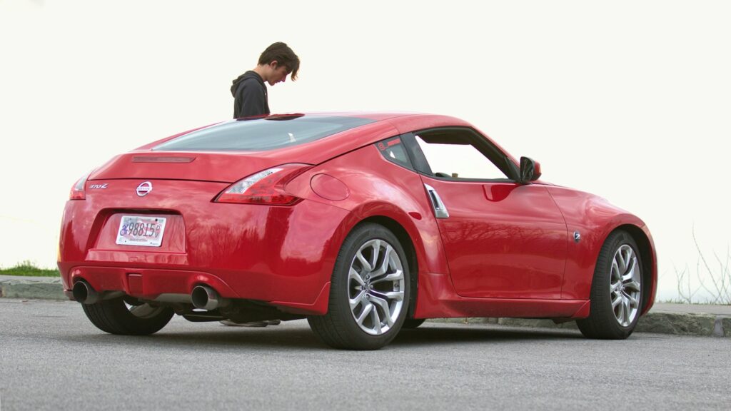 A young man leans out of a red sports car