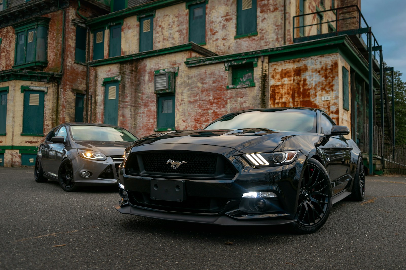A black sports car and a grey sedan parked before a weathered brick building