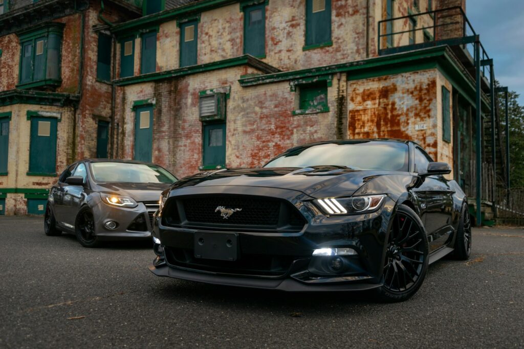 A black sports car and a grey sedan parked before a weathered brick building