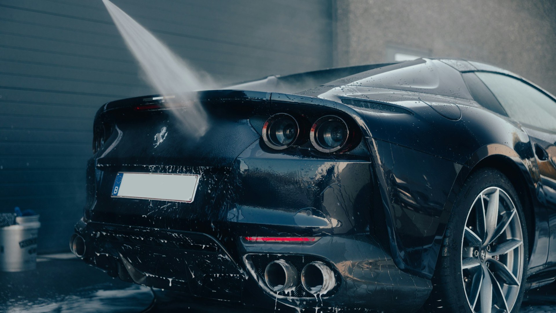 A glossy black sports car being sprayed with water in a wash bay (Unsplash photo by Lorenzo Hamers).