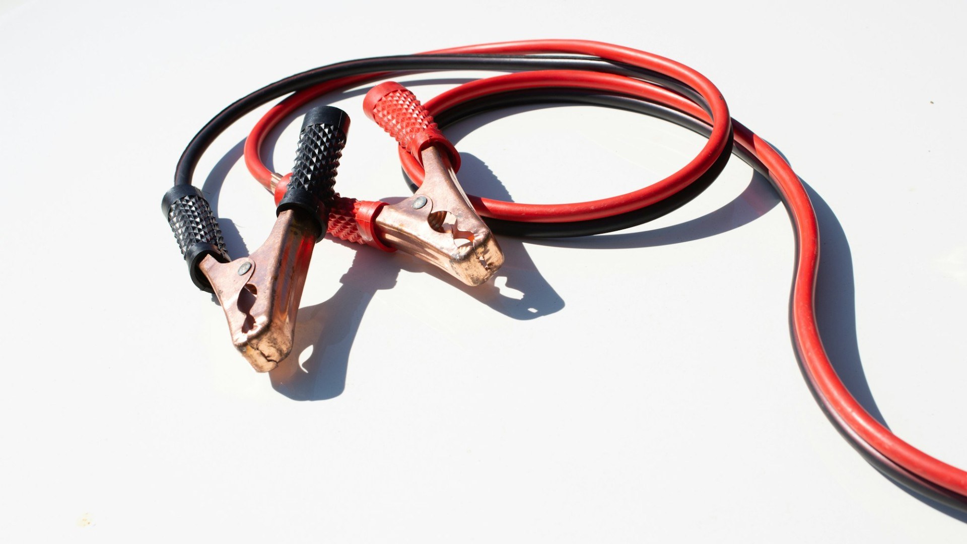 A pair of red and black jumper cables with clamps on a white background (Unsplash photo by Daniel).