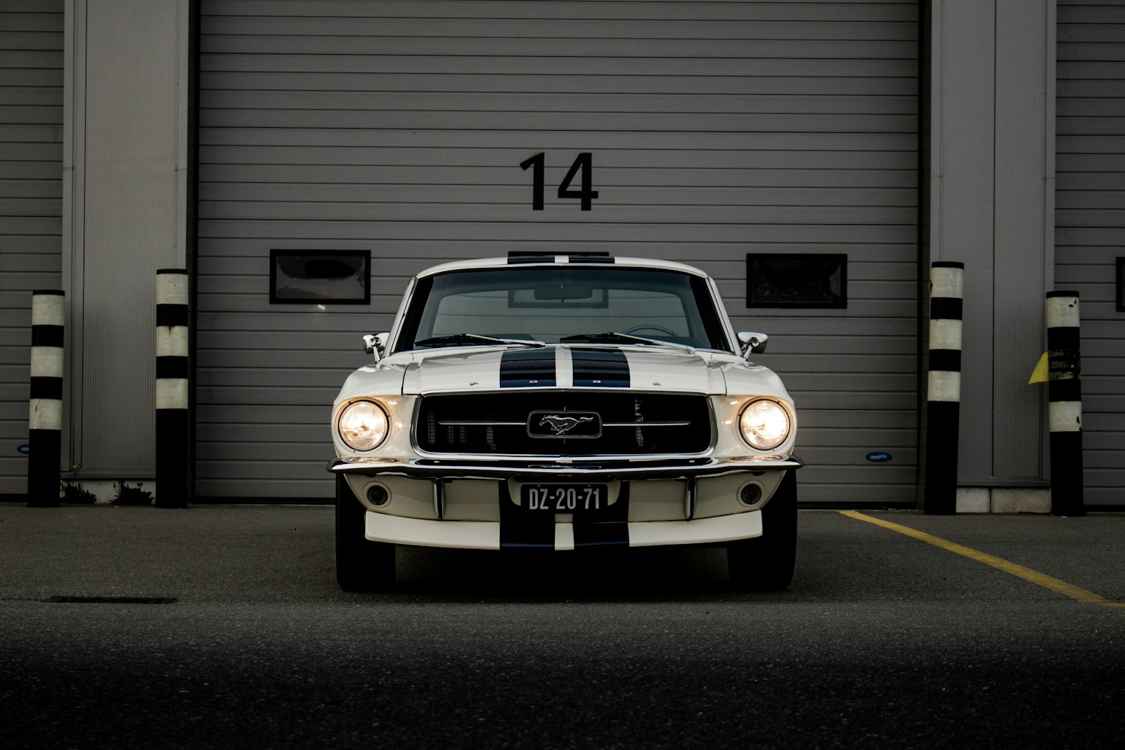 A white Ford Mustang with blue racing stripes parked before a garage door