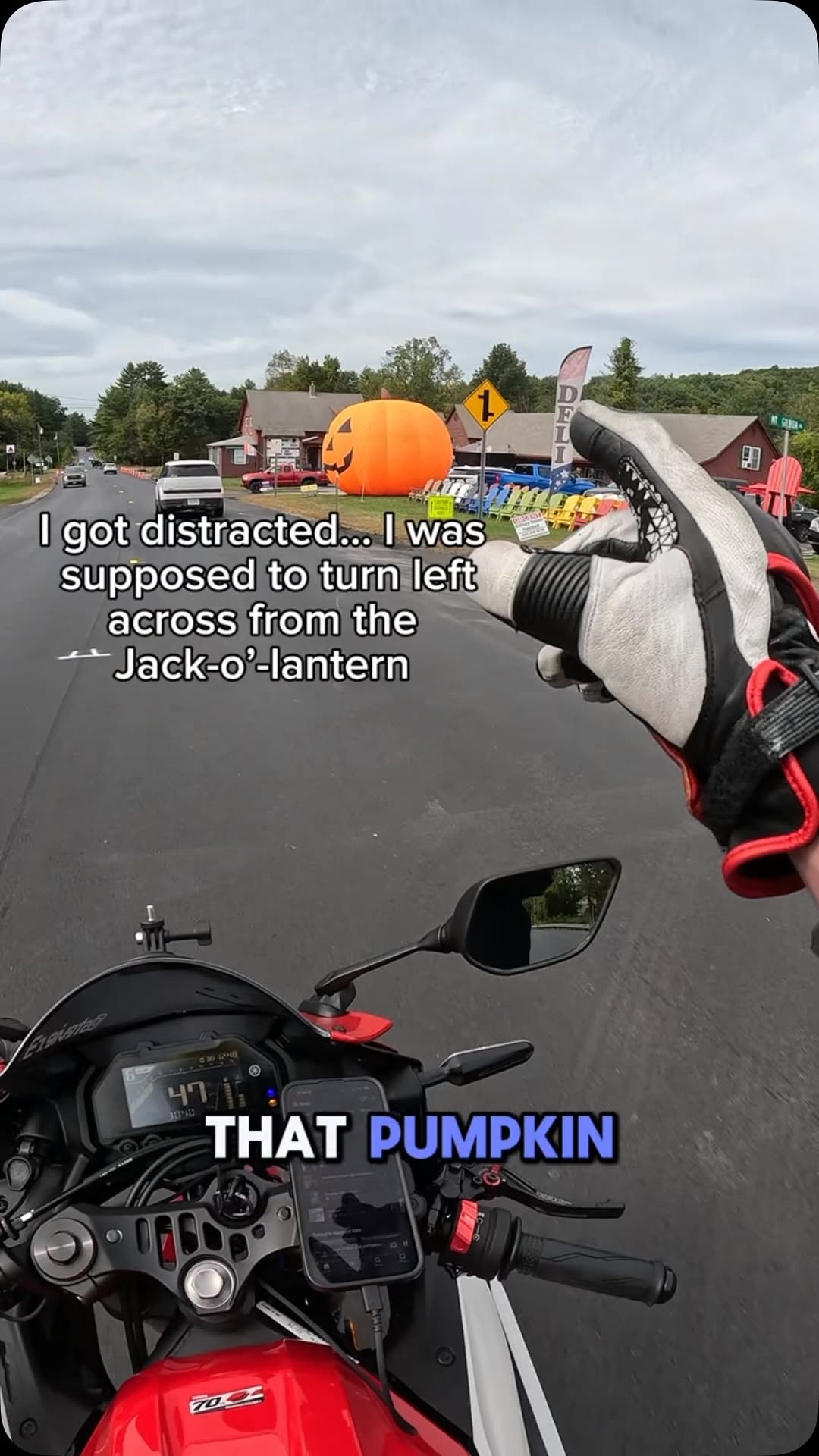 Still from an Instagram reel: a motorcyclist's view riding past a jack-o'lantern decoration beside the road.