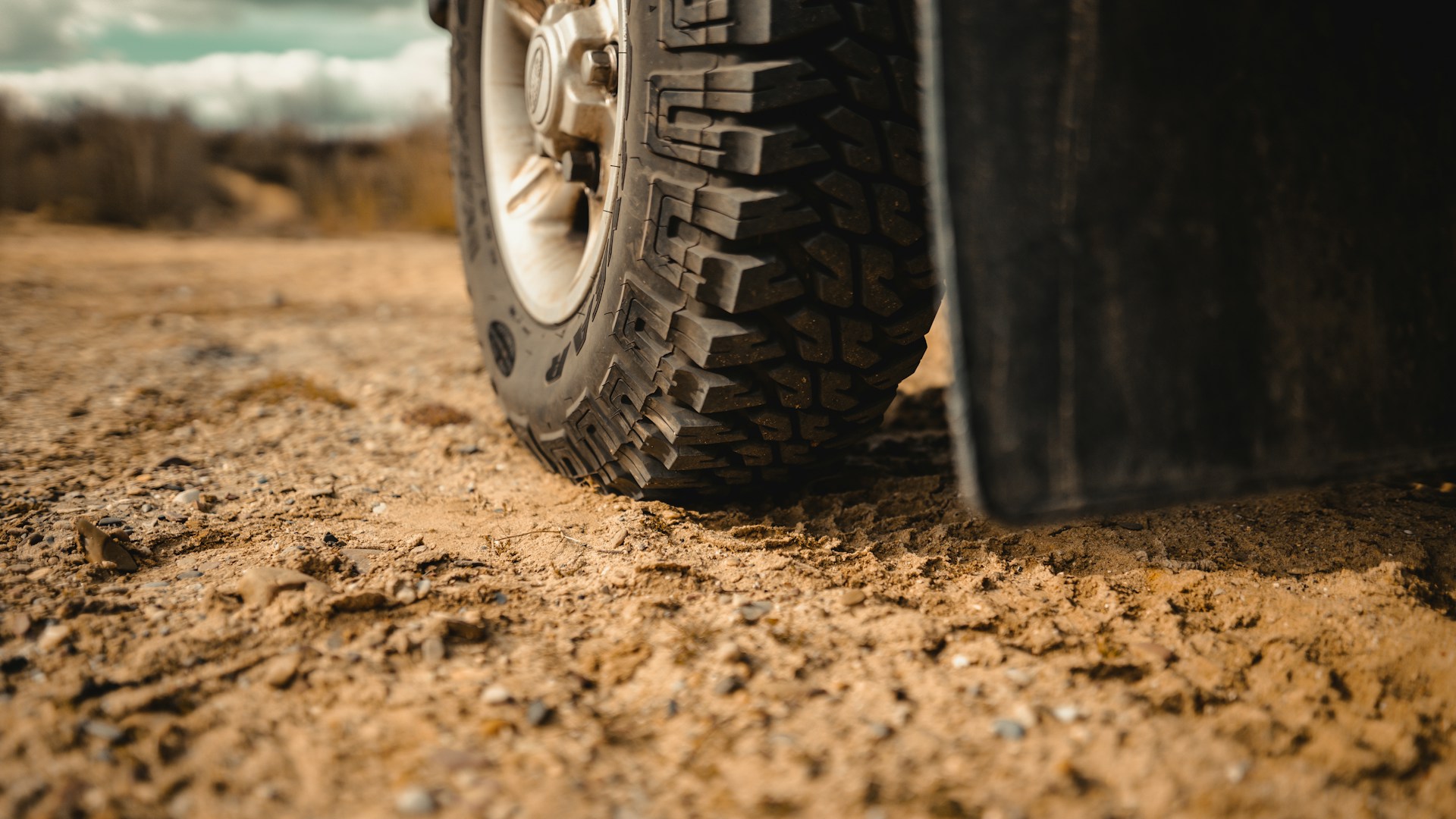 A black car tire rests on brown sand in daylight.