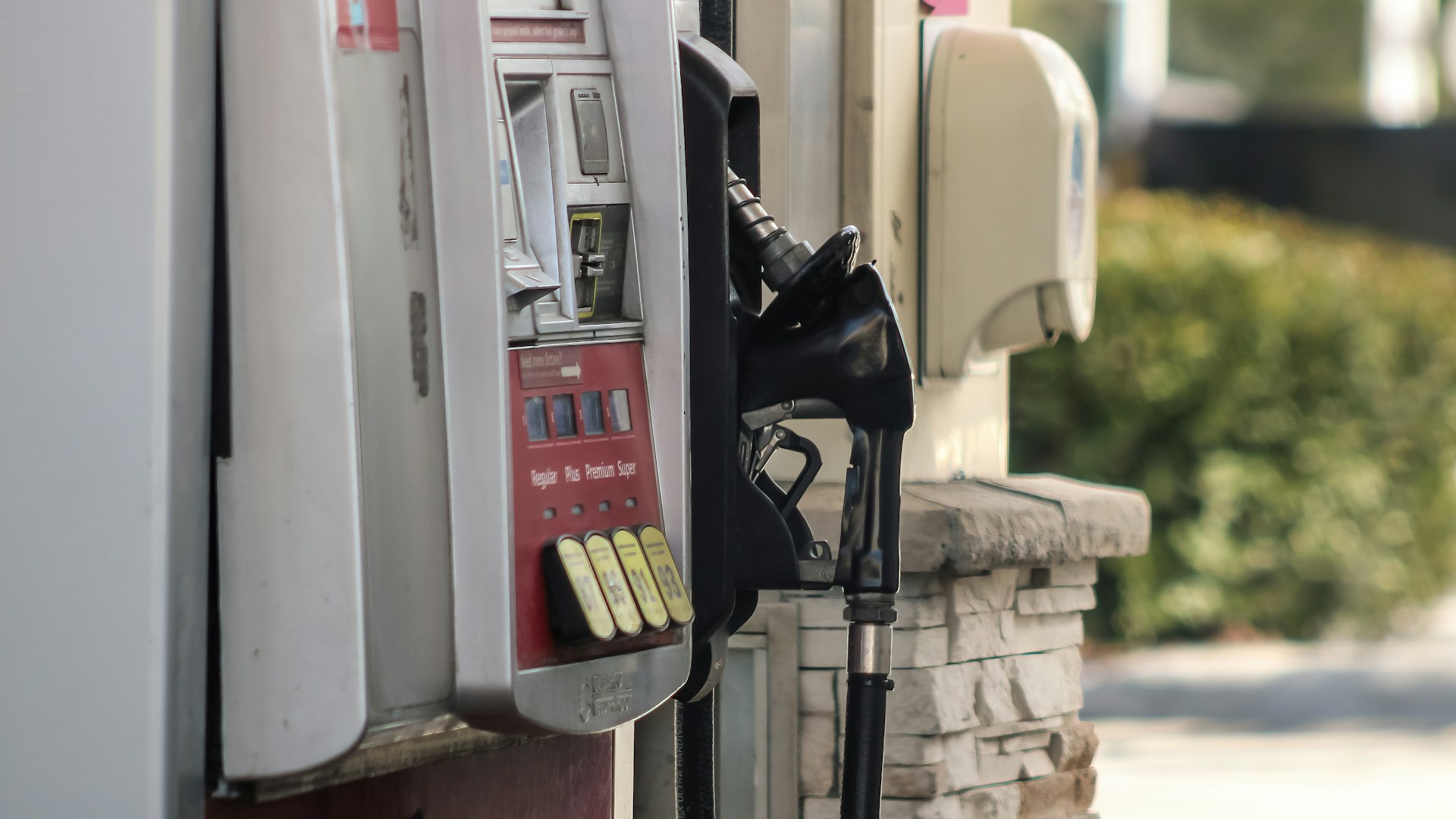 A gas pump stands next to a brick wall.