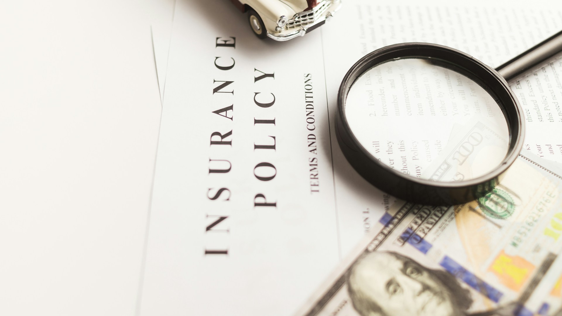 An insurance policy document with a magnifying glass, dollar bills and a toy car.