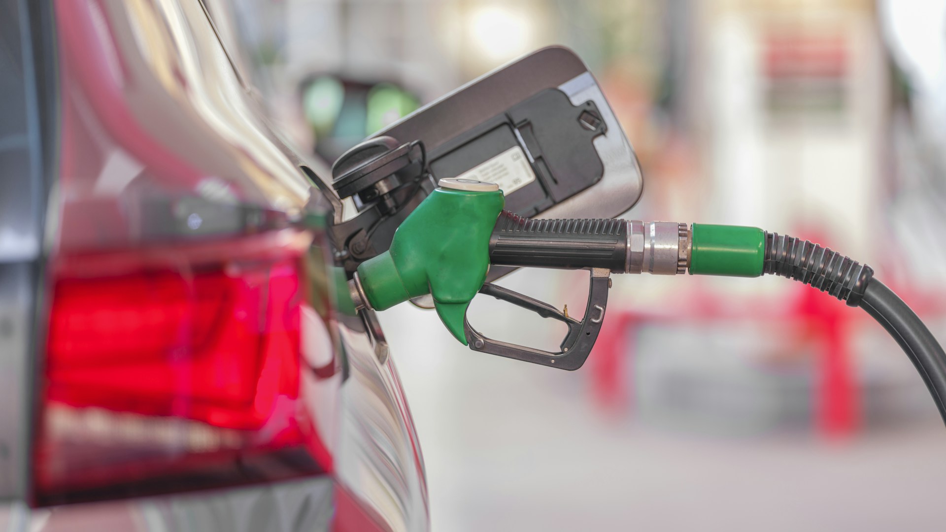 A green fuel nozzle pumping gas into a car at a gas station.
