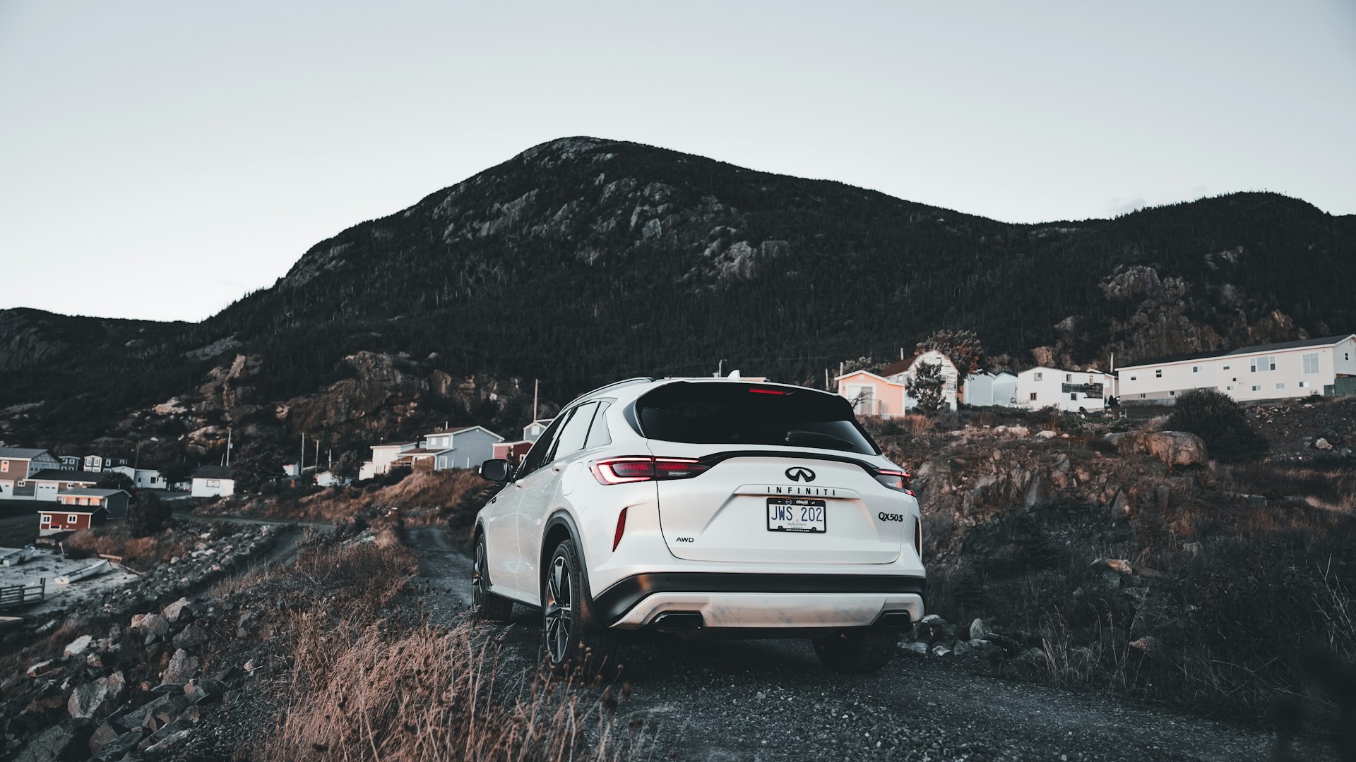 A white SUV parked on a gravel road near mountains.