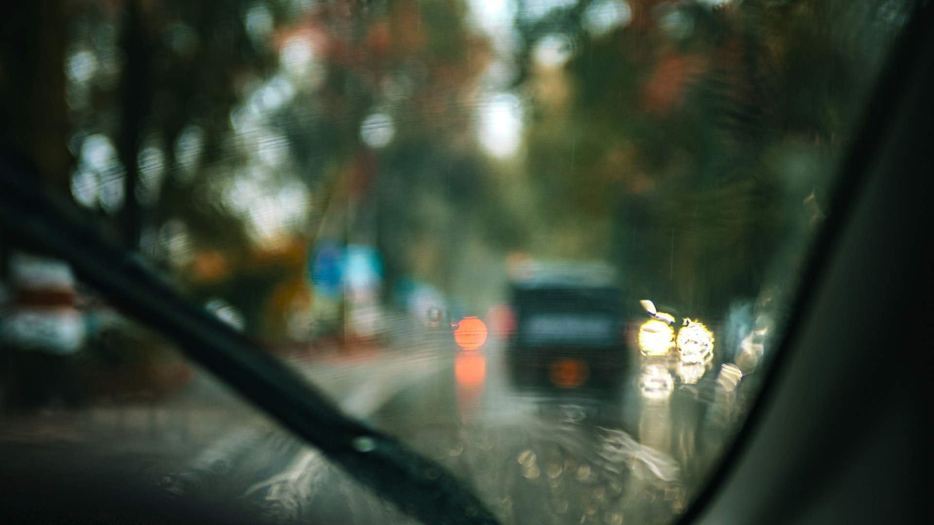 Blurred traffic lights seen through a rainy windshield.