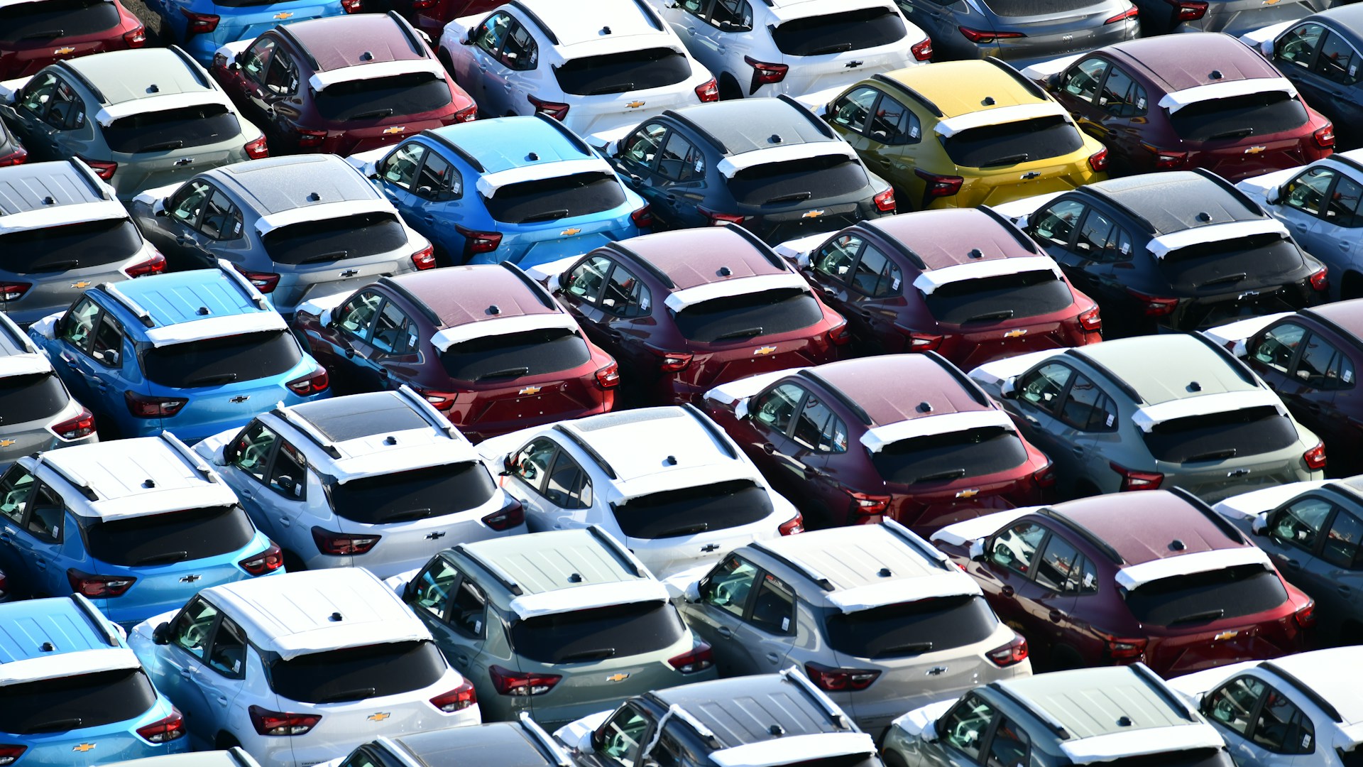Rows of new cars parked in a large dealership lot.
